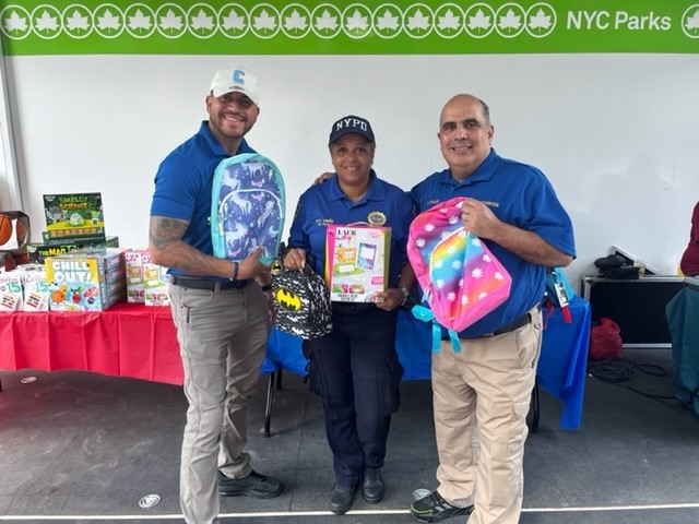 Two Public safety team members and an NYPD officer posing with school supplies.