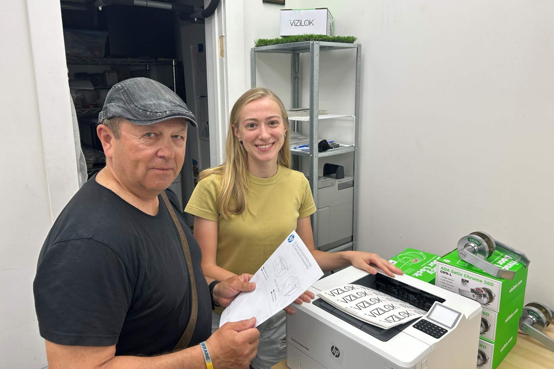 Two people gather in front of a new printer that has printed mew company logos. 