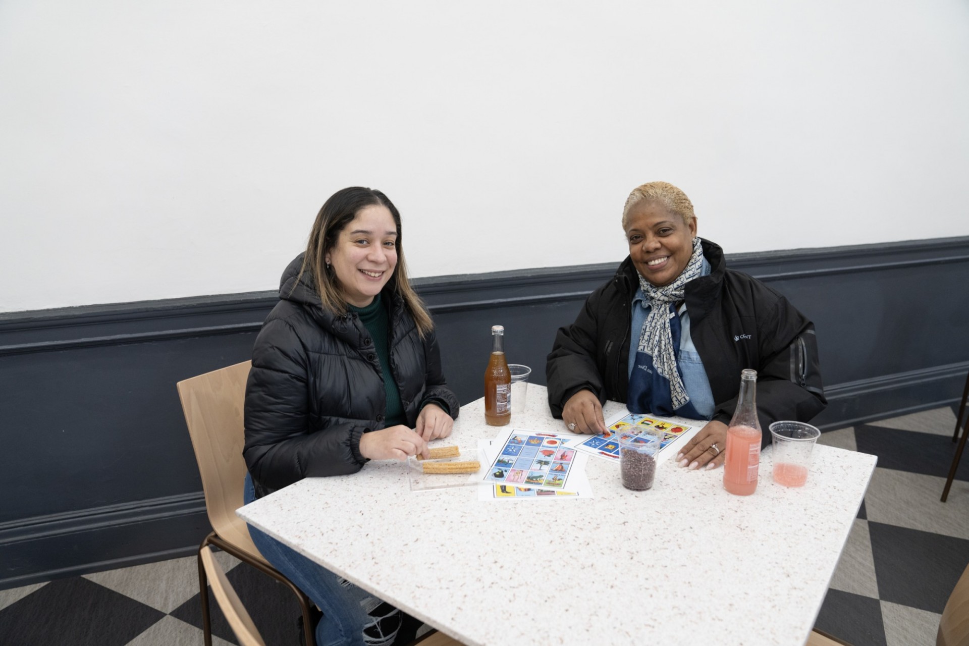 CUFO staffed played Loteria in John Jay Dining Hall. Photo by Michael DiVito. Two CUFO staff members sitting at a table together with Loteria game boards, Jarritos soda, and churros.