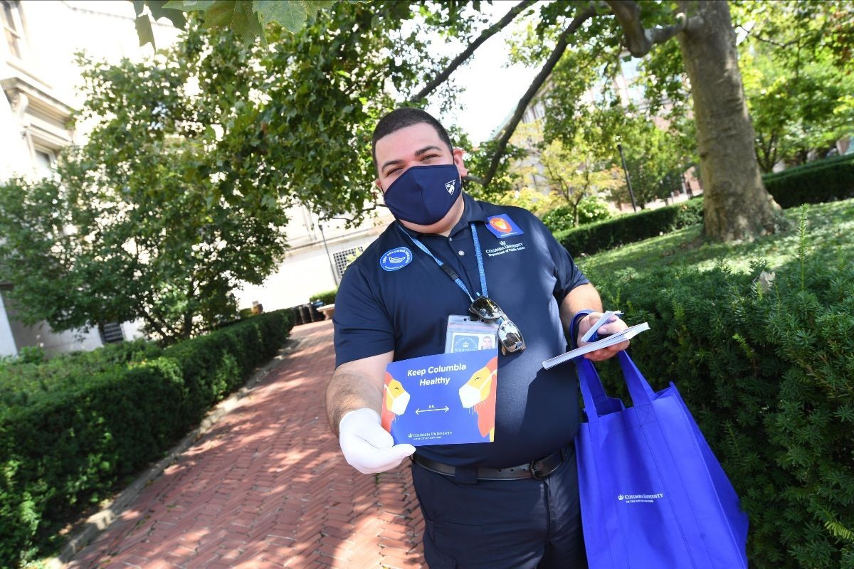 Stay Healthy Ambassador wearing a face covering and handing out postcards on campus welcoming new arrivals