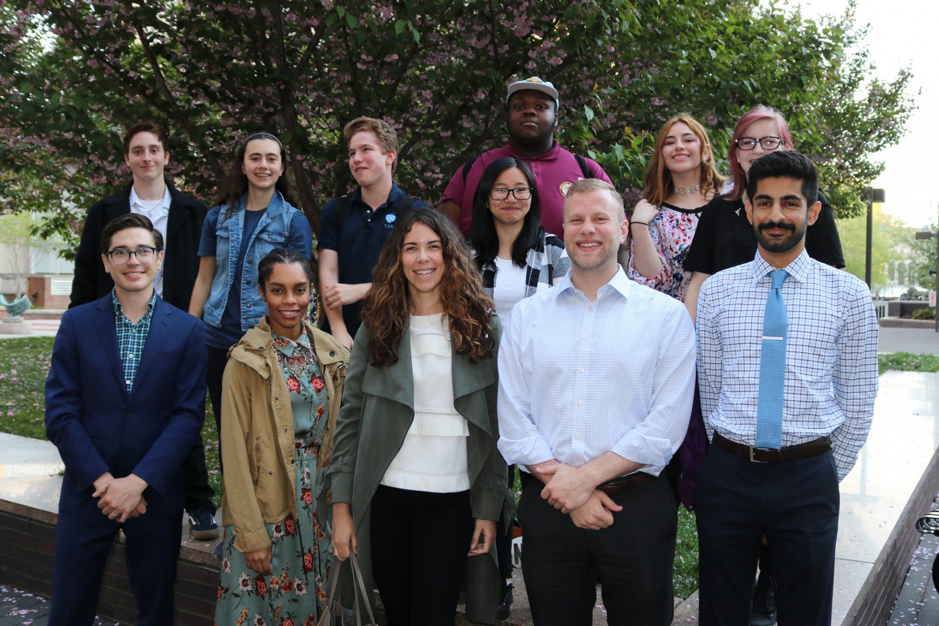 A group of students stand on a large, elevated tree pit behind a group of employees.