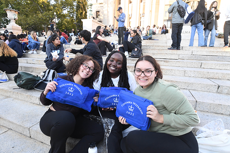 Three students sitting on Low steps holding event blankets
