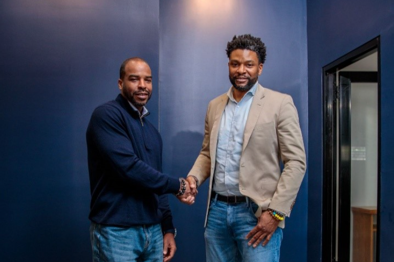 A person shakes another person's hand in a dark blue room.