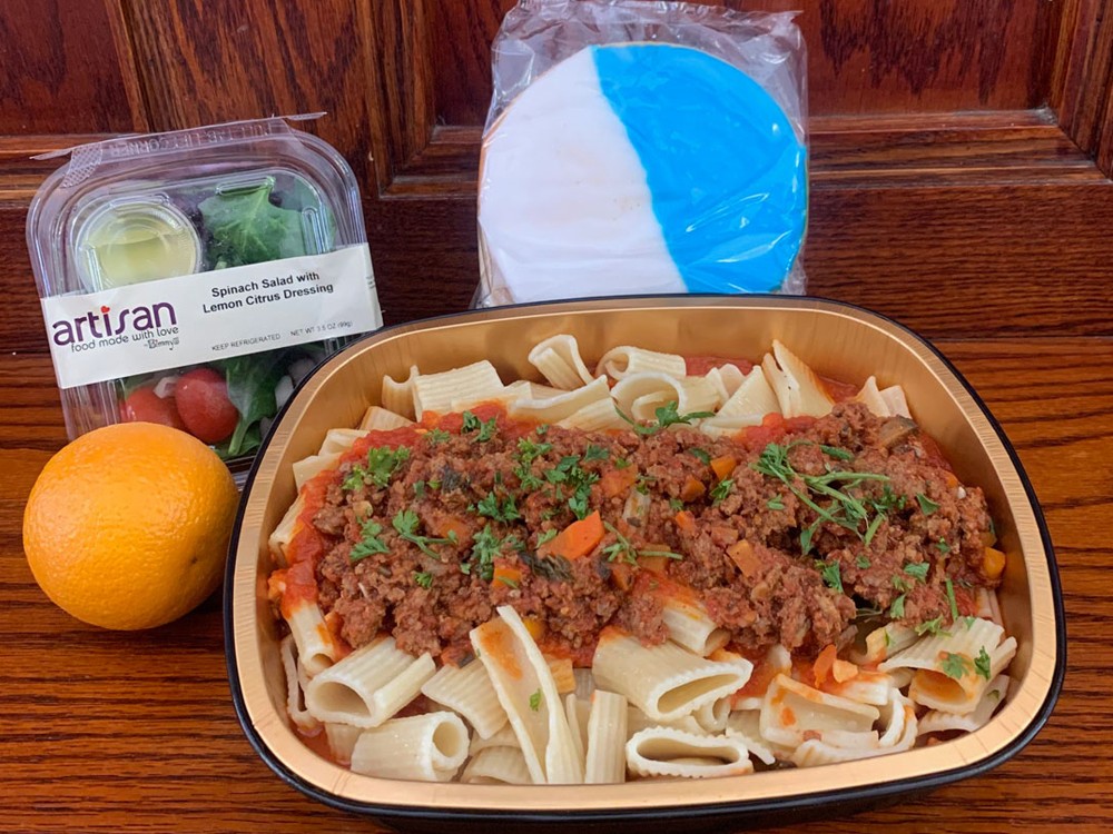 A typical meal prepared for students during the delivery period. (Photo: Campus Services) A pasta and meat sauce meal prepared for students during the delivery period, with a salad, orange, and large white and blue cookie.