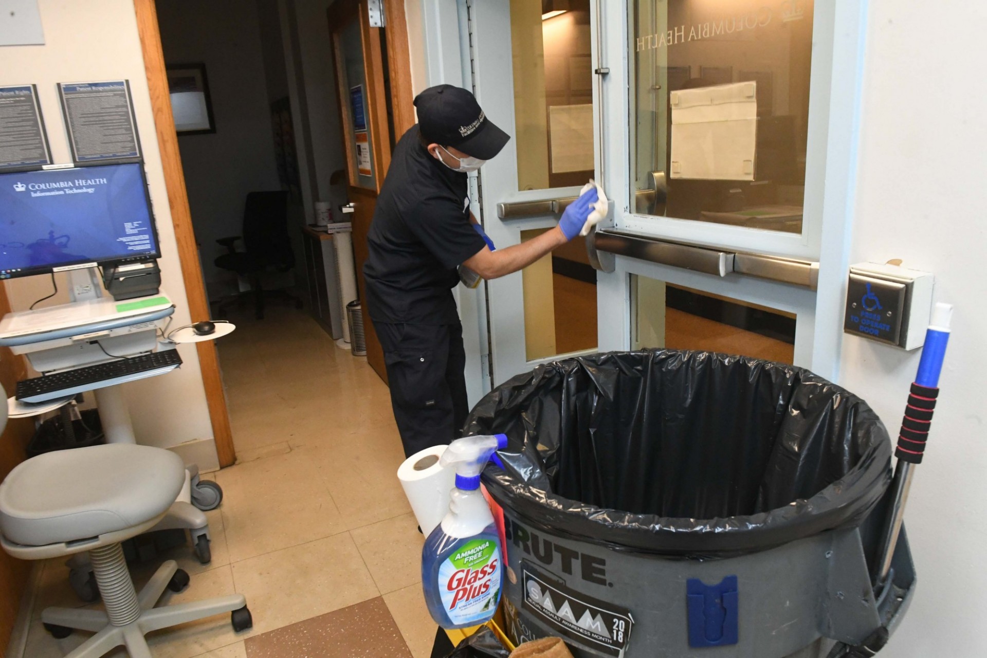 A man in a blue custodial uniform cleans the handles of a door.