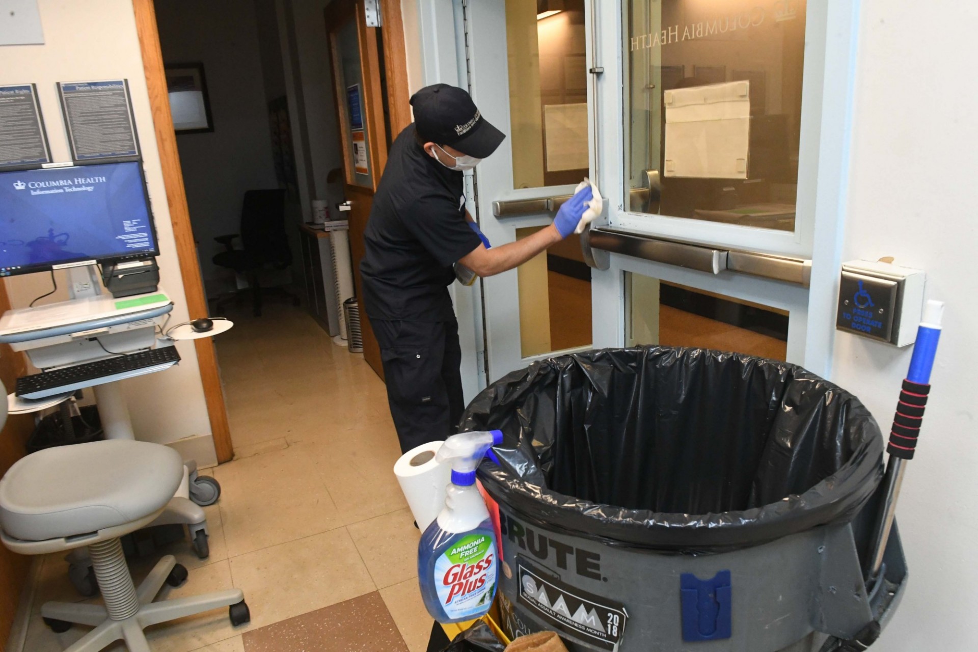 The Custodial team has increased cleanings of high-touch surface areas like door handles. Photo credit Eileen Barroso. A man in a blue custodial uniform cleans the handles of a door.