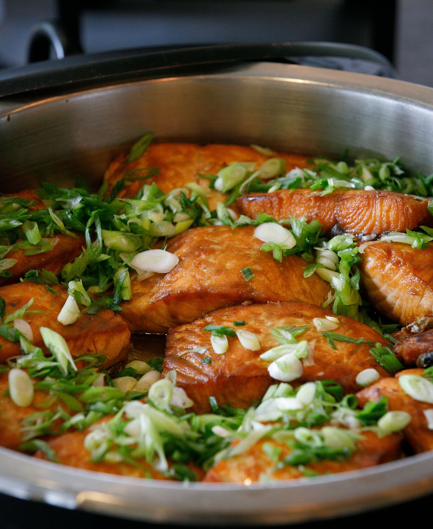 Salmon topped with green onion slices in a black serving dish.