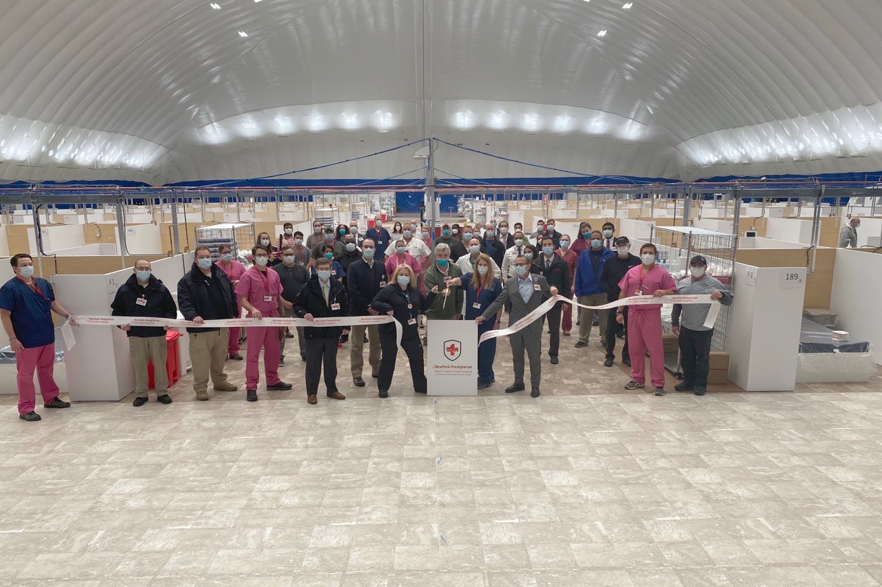 A group of people stand inside of the Bubble at Baker field hospital, holding a cut ribbon.