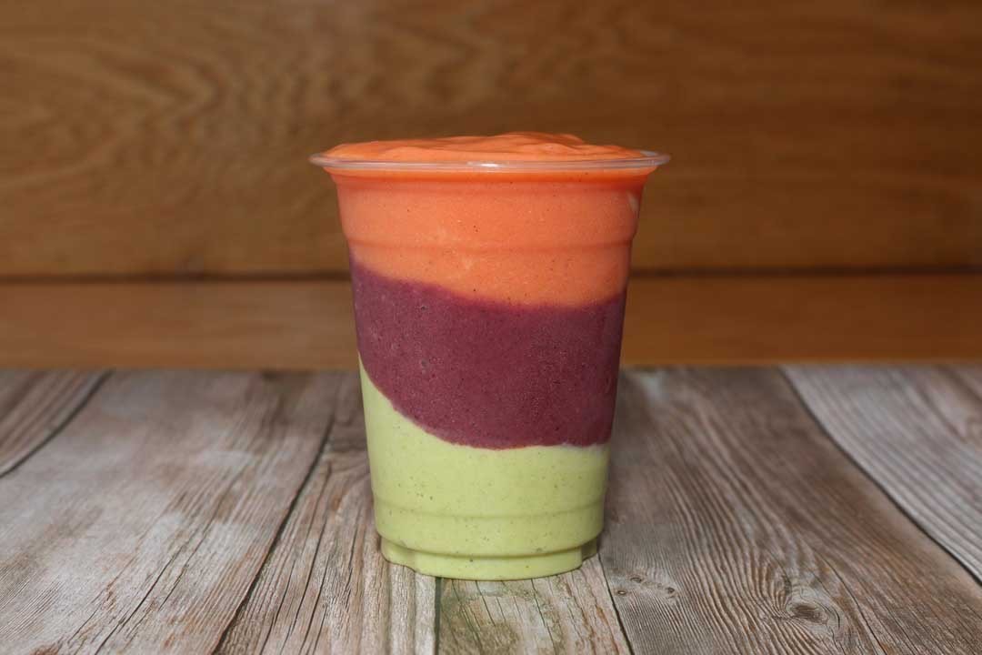 A shot of a smoothie from Oasis Jimma Juice Bar that is light green at the bottom, maroon in the middle, and orange on top.