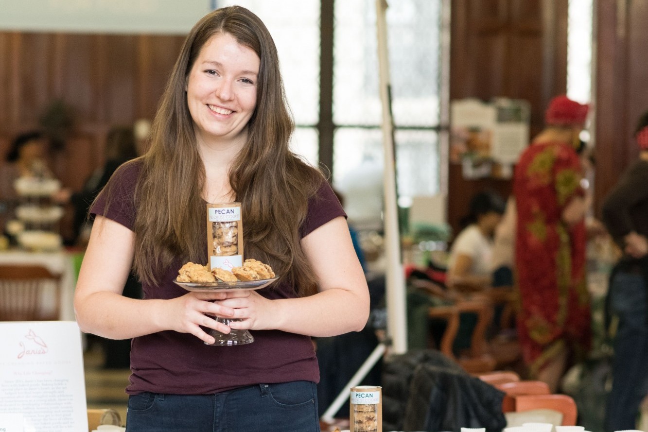 A woman stands in John Jay Dining Hall, holding a plate of cookies
