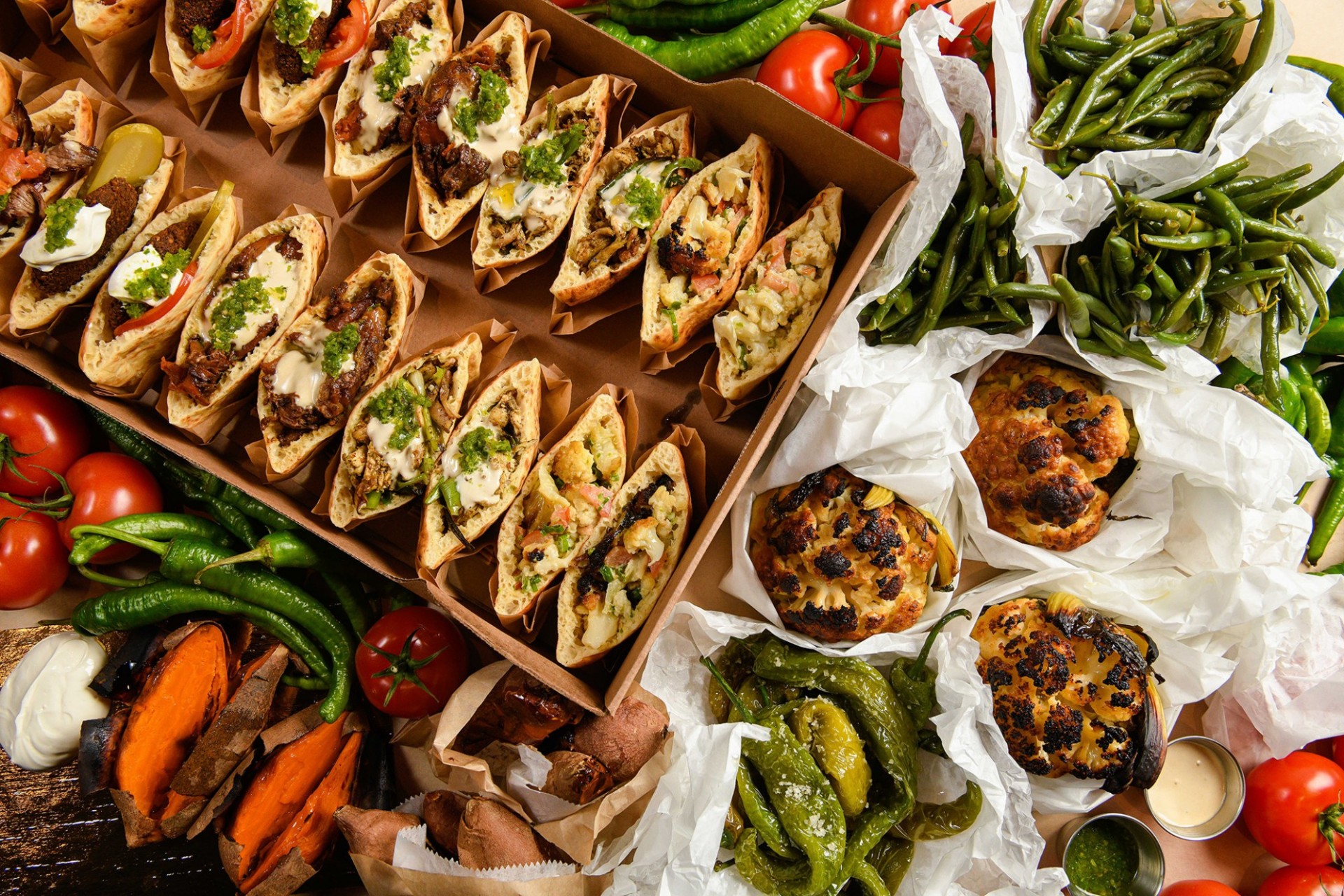 A selection of Miznon catering options, including an assortment of pitas, green beans, peppers, and baby cauliflower.