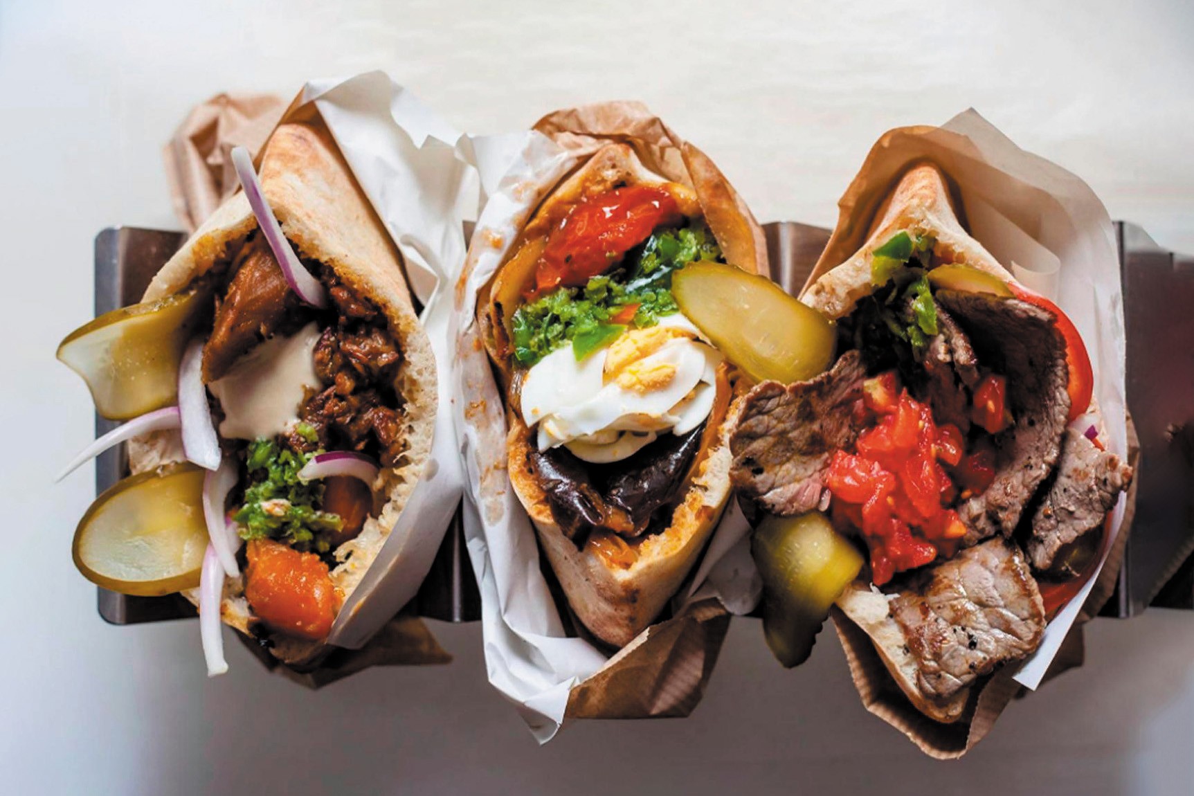 A selection of three pita entrees, with different toppings including pickles, sour cream, tomatoes, and peppers.