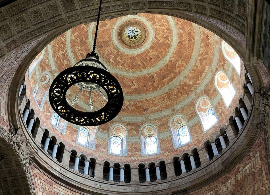 From an upward perspective, the image shows the stained glass windows that encircle the ceiling of the upper dome. Light shines through the windows.