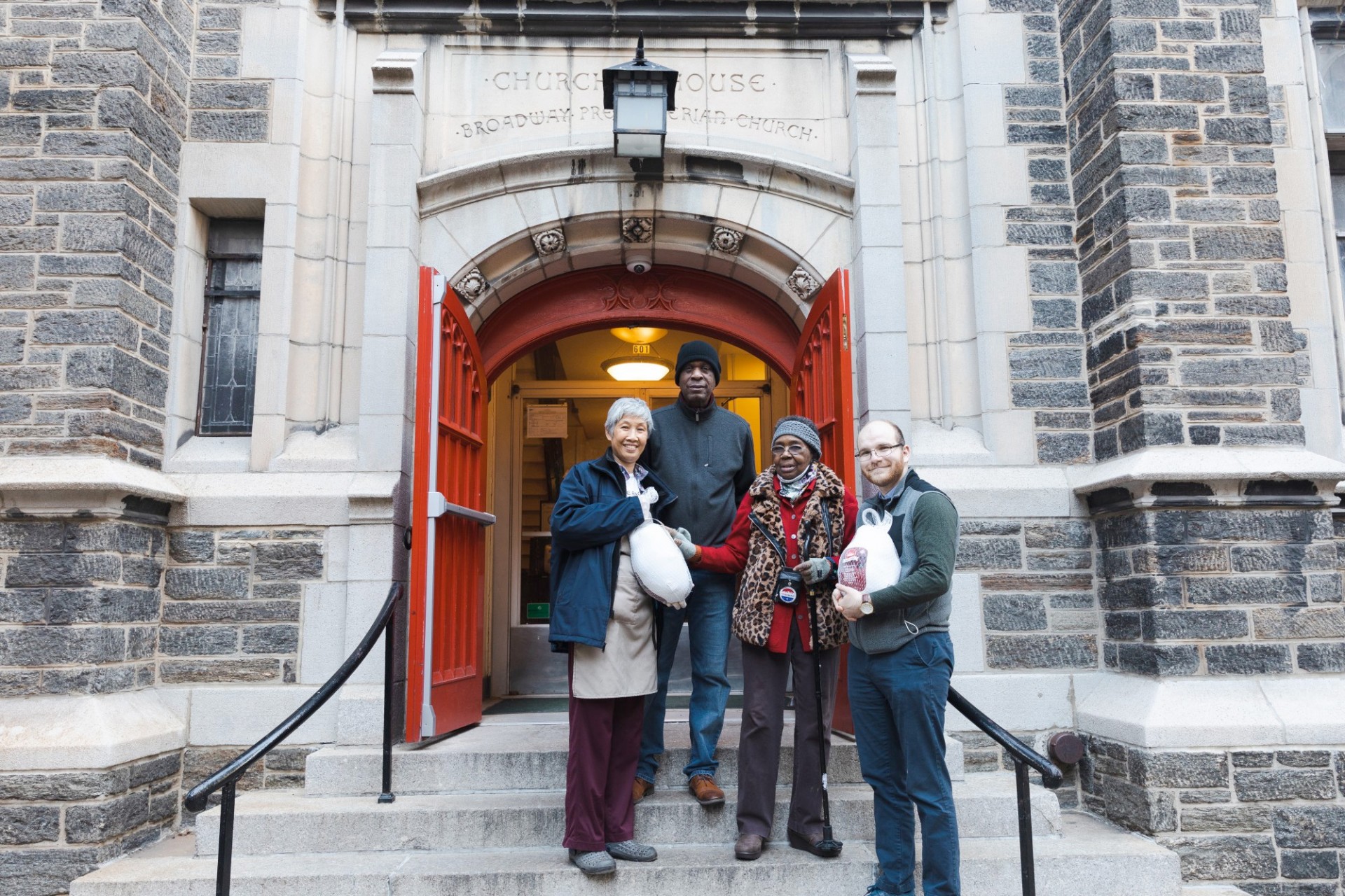 A group of people stand in front of a church, holding a turkey.