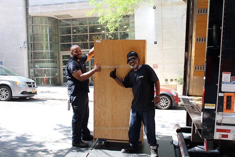 Two moving employees stand next to furniture that is being moved onto a truck.