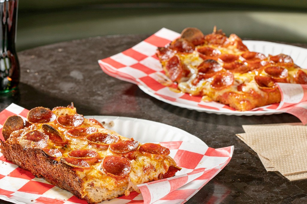 Two rectangular slices of pepperoni pizza sit on a table.  