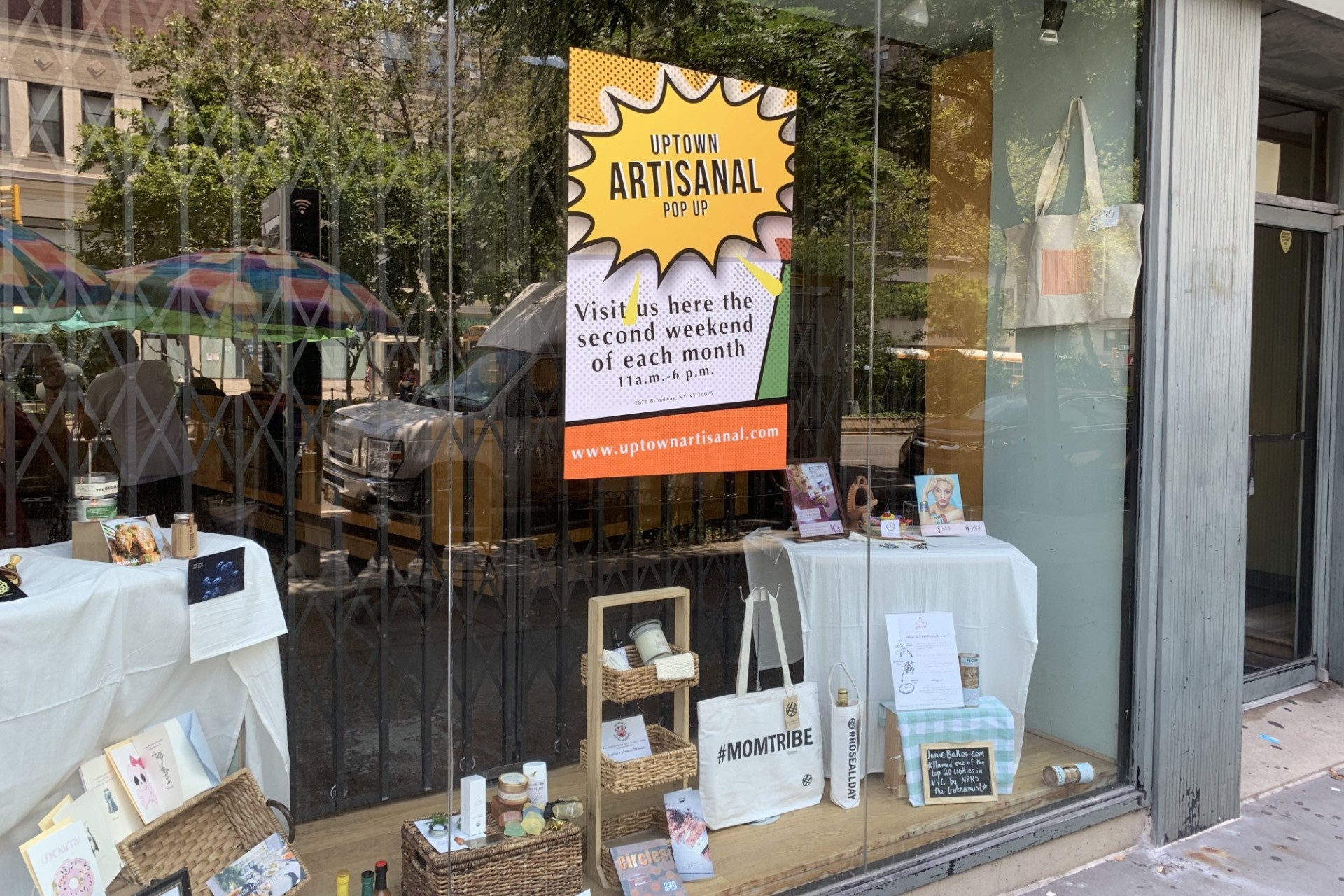 A storefront for the Uptown Artisanal pop-up market, which has a flyer and a sampling of items in the window.