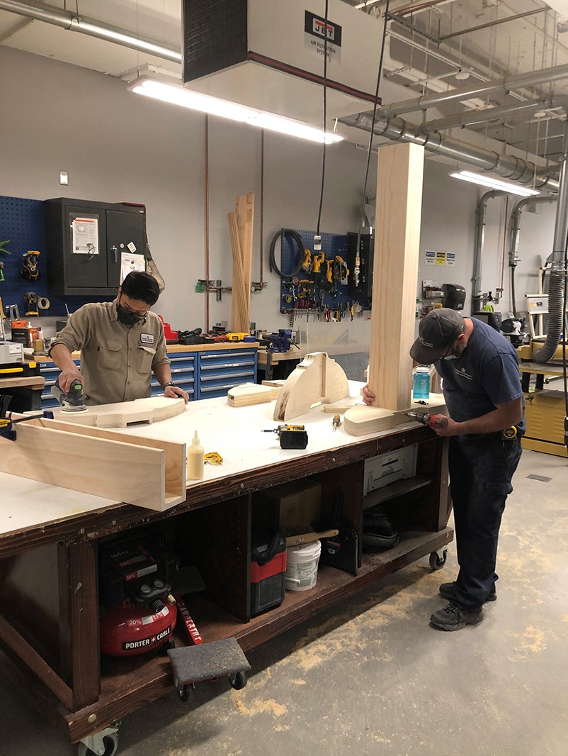 A carpenter and his apprentice from the Manhattanville Operations team assembling components of the custom frame. Two carpenters at a work bench assembling components of the custom frame for the artwork.