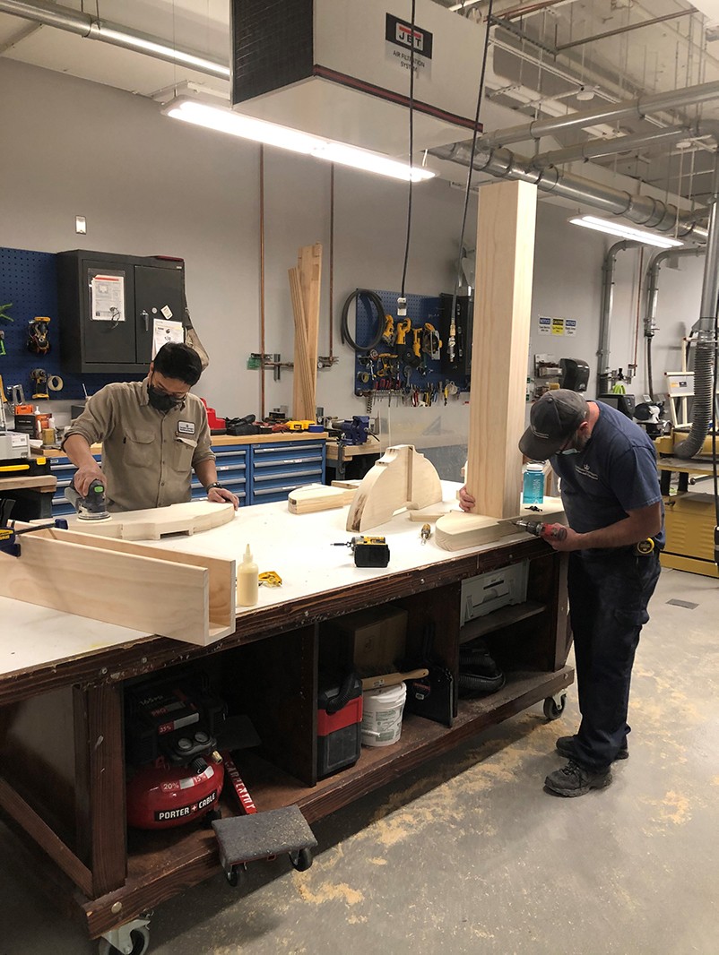 Two carpenters at a work bench assembling components of the custom frame for the artwork.