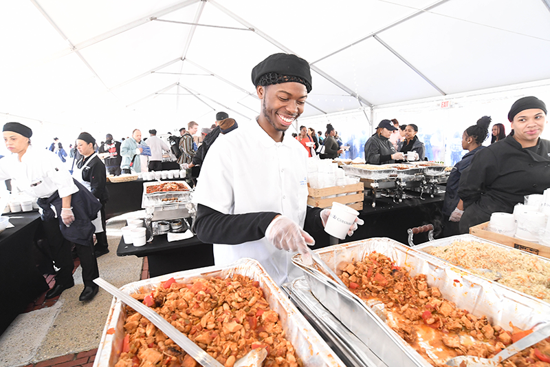 The chili is so good, Wilron can't help but smile A staff member smiles as he scoops chili into a cup