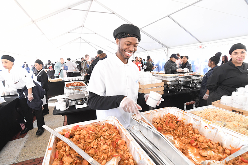 A staff member smiles as he scoops chili into a cup