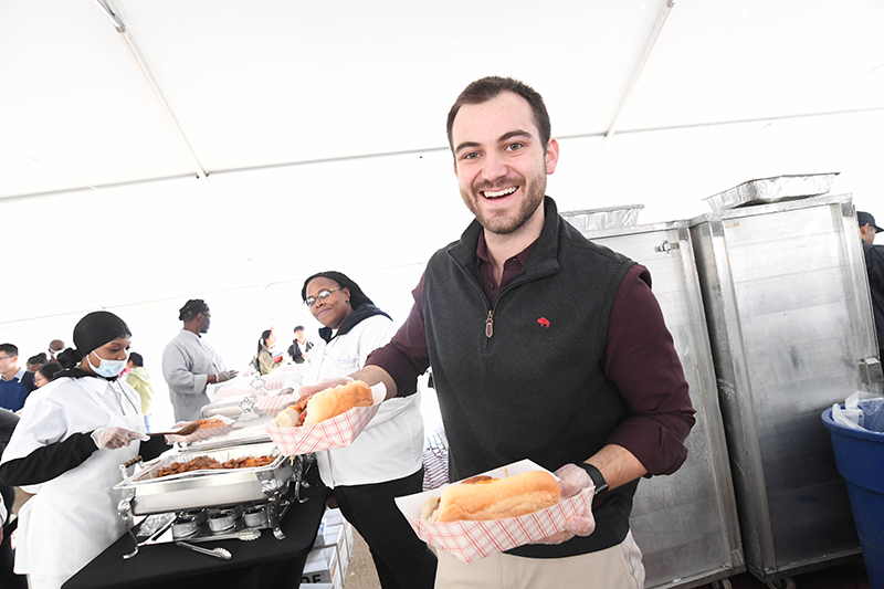 A staff member holds plates of sausages in rolls with peppers